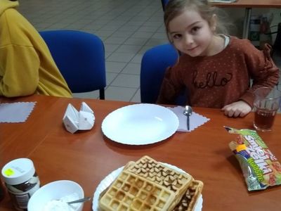Dziewczynka z Placówki Wsparcia Dziennego w Pękaninie gotowa do spożywania gofrów, które widoczne są na talerzu na pierwszym planie. 