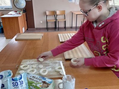 Dziewczynka z Placówki Wsparcia Dziennego w Sulechowie układająca oponki serowe na deseczce do krojenia.