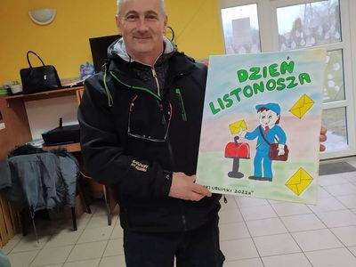 Listonosz prezentuje obraz, który otrzymał od dzieci z Placówki Wsparcia Dziennego z Lasek.
