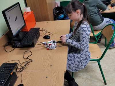 Dziewczynka przygotowuje robota do pracy na stanowisku komputerowym, z lewej strony komputer.