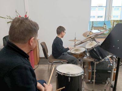 Chłopiec gra na perkusji podczas próby w Świetlicy Kultury w Malechowie. Obok jego poczynania śledzi instruktor muzyczny. 