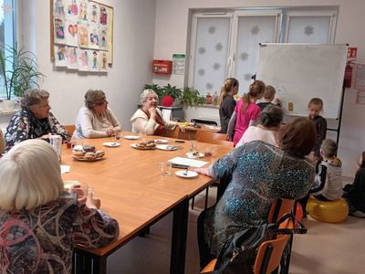 Dzieci z Placówki Wsparcia Dziennego w Ostrowcu wraz z seniorami podczas spożywania pączków.
