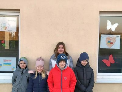 Dzieci z Podgórek przed świetlicą, pozują przy pracach plastycznych wyeksponowanych na oknach. 