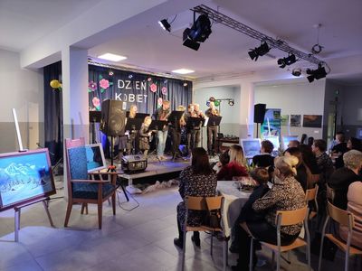 Orkiestra z Malechowa na scenie daje koncert z okazji Dnia Kobiet, który oglądają zgromadzone w Świetlicy Kultury Panie.