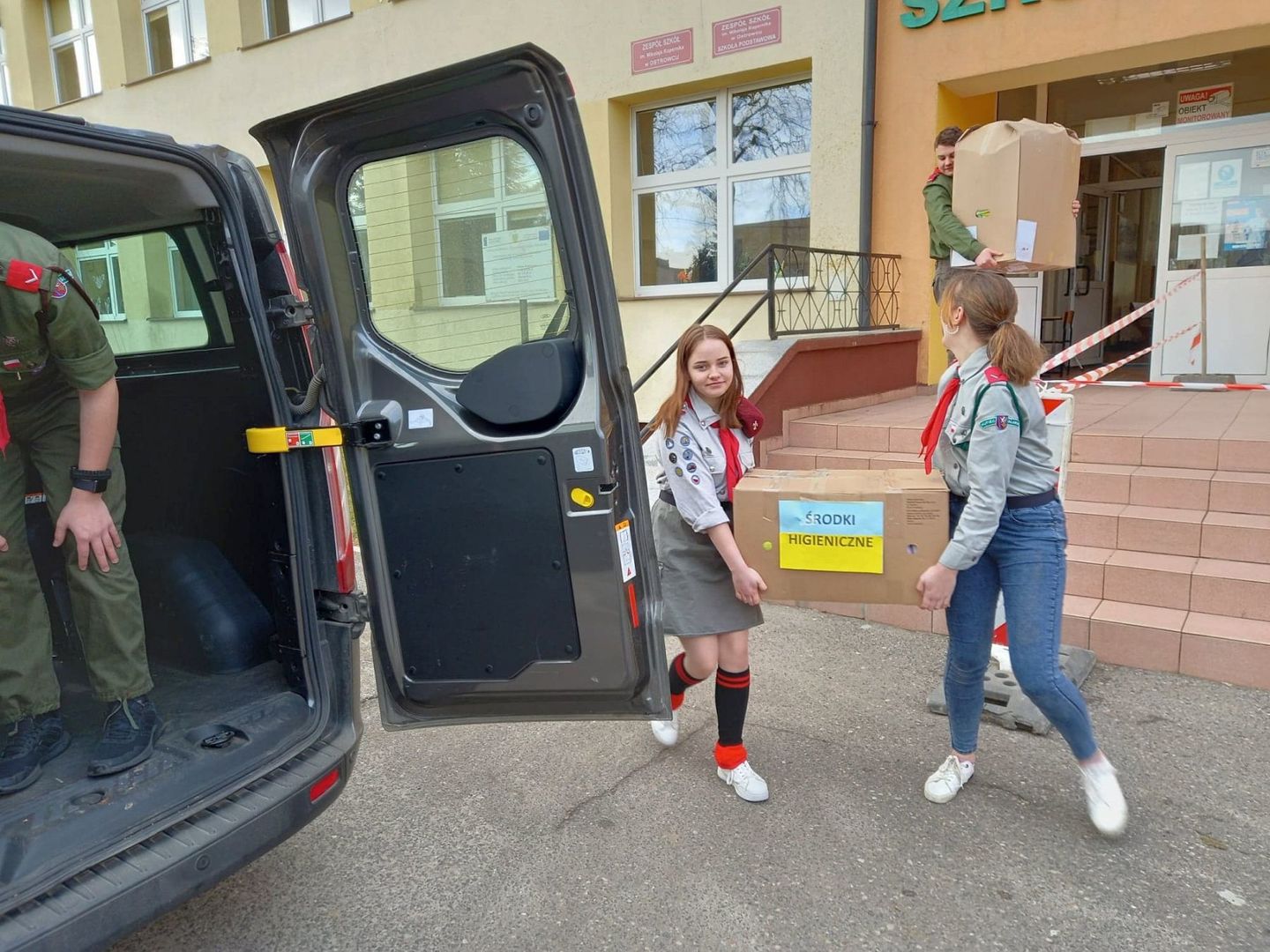 Harcerki z Ostrowca przenoszą kartony z zebranymi materiałami dla Ukraińców z busa do budynku szkoły.