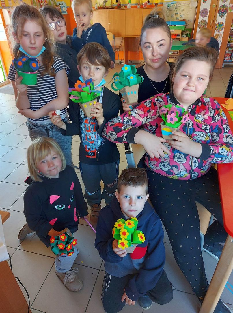 Dzieci z Placówki Wsparcia Dziennego z Lasek wraz z wychowawczynią prezentują wykonane kwiaty z papieru.
