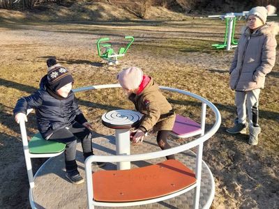 Troje dzieci z PWD w Sulechowie bawiących się na placu zabaw. Dziewczynka i chłopiec kręcą się na karuzeli, obok nich stoi starsza dziewczynka.