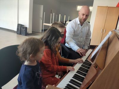 Instruktor przy pianinie i troje dzieci podczas lekcji.