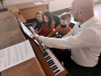 Instruktor uczy troje dzieci gry na pianinie.