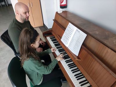 Instruktor uczy dziewczynkę gry na pianinie. 