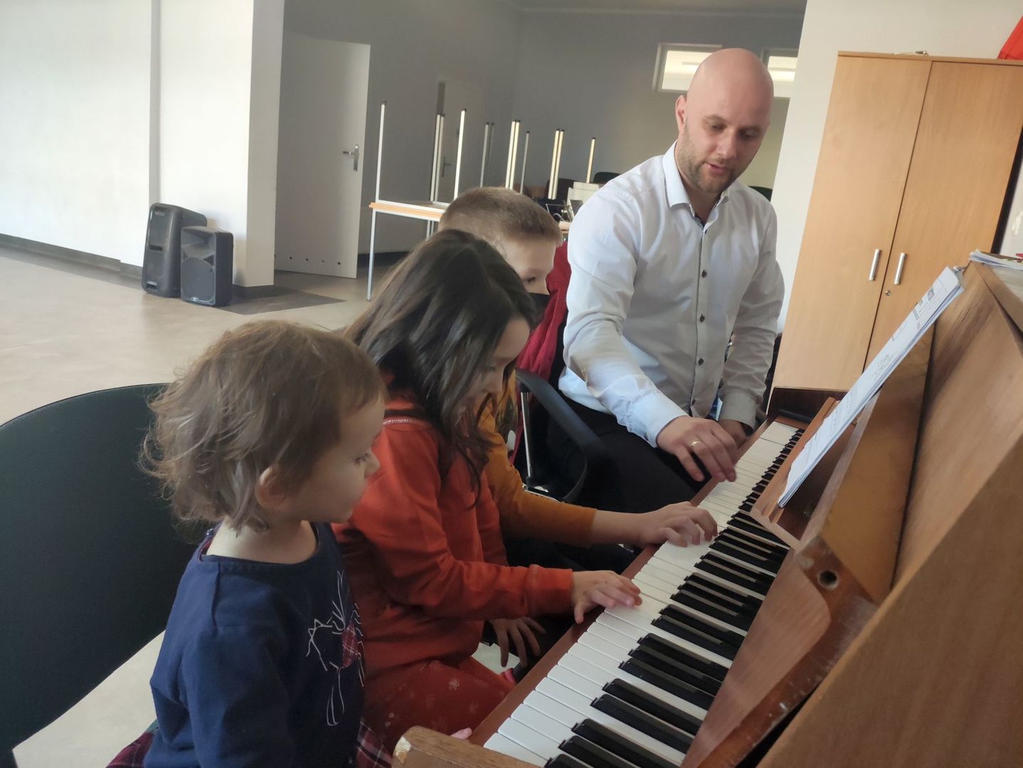 Instruktor przy pianinie i troje dzieci podczas lekcji.