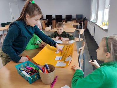 Dzieci ze starszej grupy podpisują plakat z podstawowymi zwrotami w języku angielskim. 