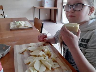 Dziewczynka z Placówki Wsparcia Dziennego w Sulechowie krojąca jabłka. Na stole deski do krojenia i jabłka.