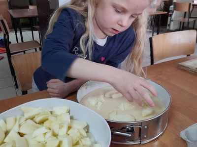 Dziewczynka z Placówki Wsparcia Dziennego w Sulechowie układająca kawałki jabłek na przygotowanym do upieczenia cieście biszkoptowym.
