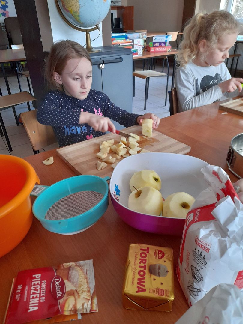 Dwie dziewczynki z PWD w Sulechowie krojące jabłka. Na stole widać jabłka, mąkę, margarynę, proszek do pieczenia.