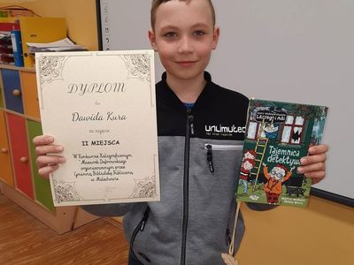 Filalista konkursu kaligraficznego prezentuje dyplom oraz nagrodę.