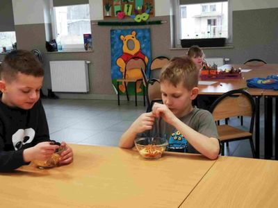 Dwaj chłopcy z Placówki Wsparcia Dziennego w Kusicach podczas jedzenia spaghetti, na drugim planie dziewczynka.