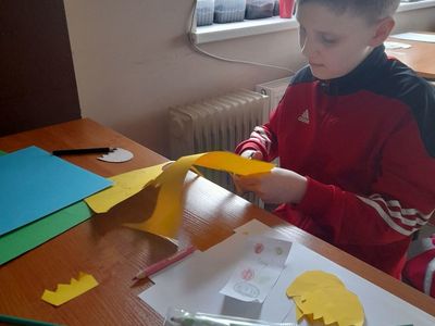 Chłopiec z Placówki Wsparcia Dziennego w Sulechowie wycinający kwiaty z kolorowego papieru. Na stoliku widać kredki i kolorowy papier.