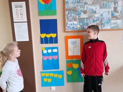 Dziewczynka i chłopiec z Placówki Wsparcia Dziennego w Sulechowie prezentujący galerię prac przedstawiającą wiosenne kwiaty.