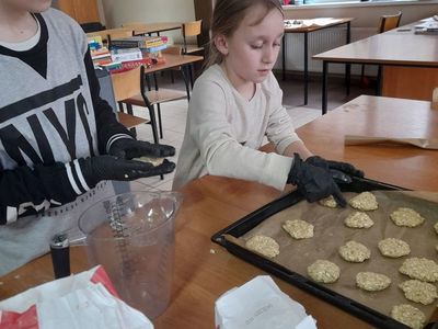 Chłopiec i dziewczynka z Placówki Wsparcia Dziennego w Sulechowie formujący ciasteczka owsiane i układający je na blaszce do pieczenia.Na stole widać produkty spożywcze.