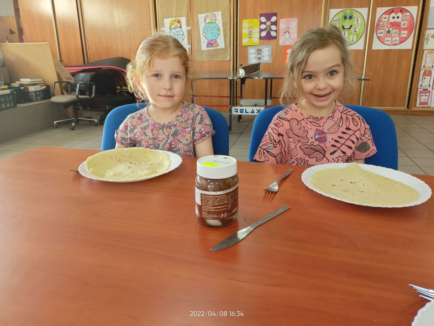 Dwie dziewczynki z Placówki Wsparcia Dziennego w Pękaninie przy stole, gotowe do jedzenia naleśników.