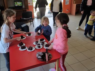 Dzieci z Placówki Wsparcia Dziennego w Laskach kroją na kawałki upieczone ciasto czekoladowe. 