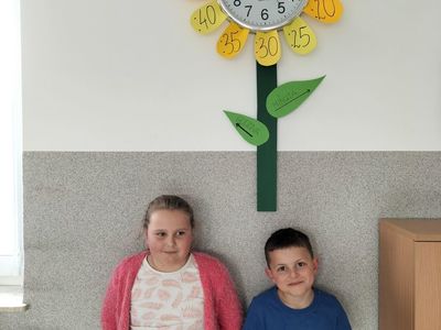 Dzieci z Placówki Wsparcia Dziennego w Kusicach przed zegarem w kształcie kwiatka. 