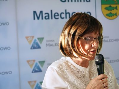 Elżbieta Aniela Kamińska odczytuje wiersz na tle ścianki promocyjnej Gminy Malechowo.