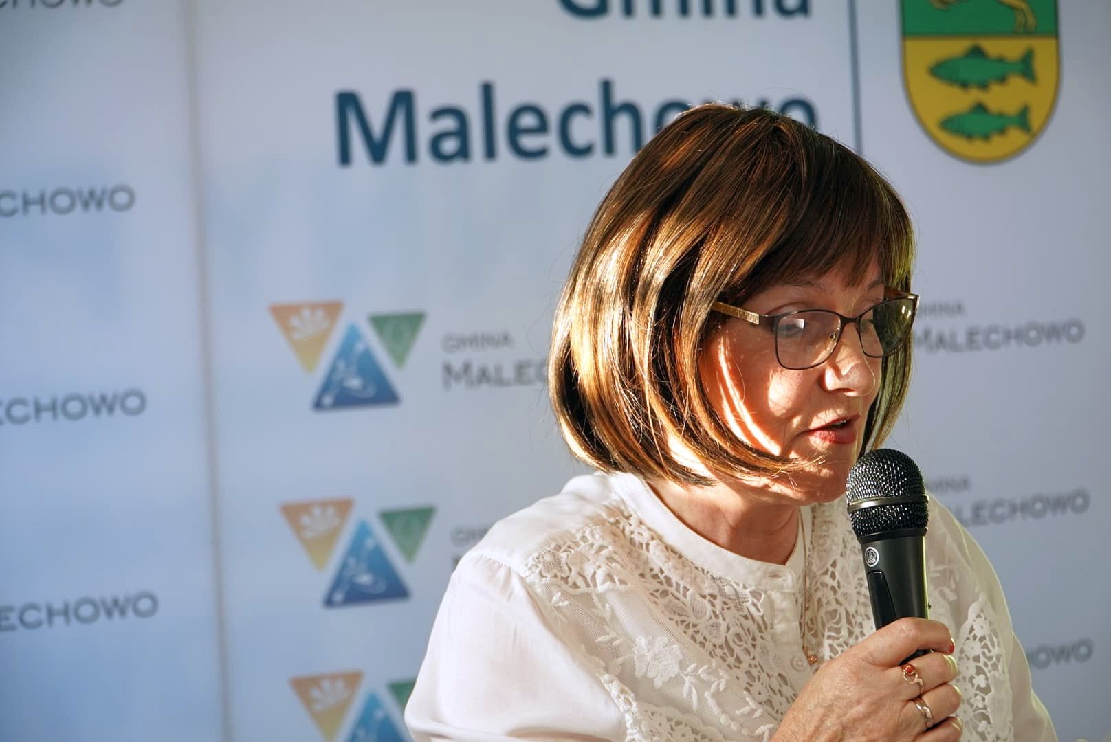 Elżbieta Aniela Kamińska odczytuje wiersz na tle ścianki promocyjnej Gminy Malechowo. 