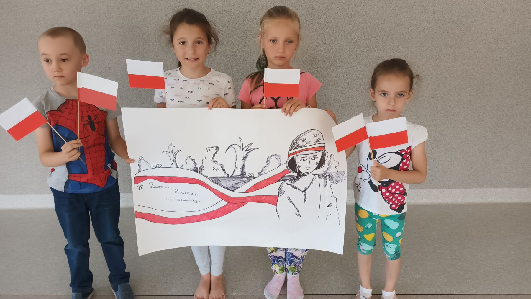 Dzieci z Placówki Wsparcia Dziennego w Ostrowcu prezentują wykonany plakat i flagi biało - czerwone.