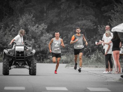 Dwaj biegacze przy stacji nawadniającej i społeczność Paprotek, przed nimi pilot na quadzie.