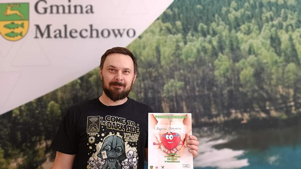 Dawca pozuje z dyplomem na tle ścianki Gminy Malechowo.