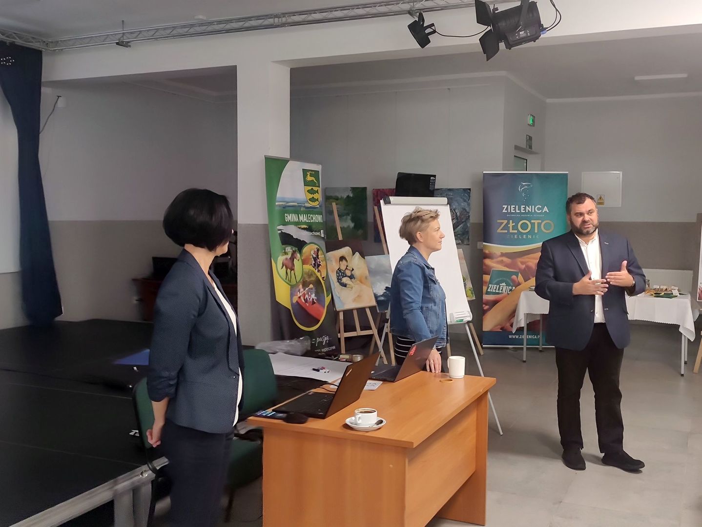 Wójt Radosław Nowakowski wita przybyłych gości, obok dwie panie prowadzące spotkanie.