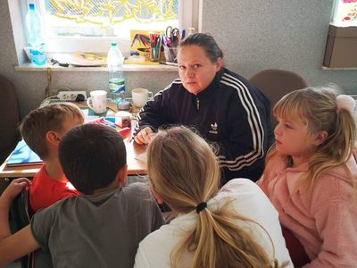 Wychowawca Placówki Wsparcia Dziennego tłumaczy dzieciom zagadnienie w ramach pomocy w odrabianiu lekcji.