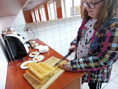 Wychowanka Placówki Wsparcia Dziennego w Laskach kroi chleb na kromki.
