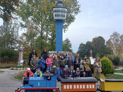 Uczniowie kl. I-III ZS w Ostrowcu wraz z opiekunami na tle latarni morskiej i miniatury kolejki w Parku Miniatur i Kolei w Dziwnowie