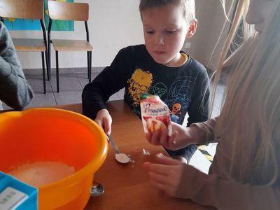 Chłopiec z Placówki Wsparcia Dziennego w Sulechowie odmierza proszek do pieczenia łyżeczką, dziewczynka mu pomaga.