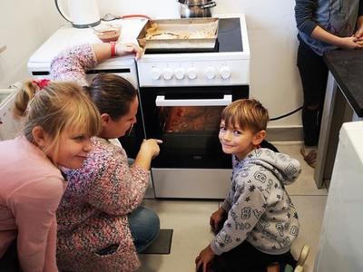 Dzieci z Placówki Wsparcia Dziennego w Kusicach z wychowawcą podczas zajęć kulinarnych, przygotowują składniki do minipizzerek. 