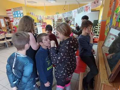 Dzieci z Placówki Wsparcia Dziennego z Lasek malują twarze kolorowymi farbkami. 