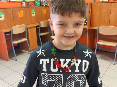 Chłopiec z PWD Laski pozuje do zdjęcia z kolorowym naszyjnikiem. 