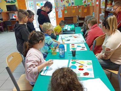 Wychowankowie z Placówki Wsparcia Dziennego z Lasek wykonują tematyczny plakat kolorowymi farbami.