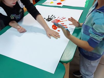 Wychowankowie z Placówki Wsparcia Dziennego z Lasek odbijają pomalowane dłonie farbami na brystolu.