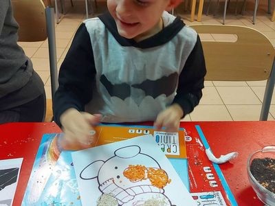 Wychowanek z Placówki Wsparcia Dziennego z Lasek wykonuje obraz z kaszy, maku, soczewicy i kleju.
