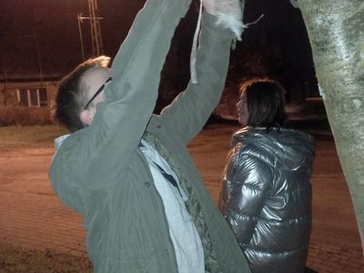 Wychowankowie z Placówki Wsparcia Dziennego z Lasek zawieszają kule ziaren i smalcu dla ptaków na drzewie