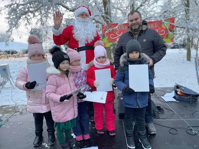 Zdjęcie laureatów konkursu na Kartkę Bożonarodzeniową na scenie z Mikołajem i wójtem Radosławem Nowakowskim.