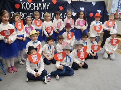 Zdjęcie przedstawia przedszkolaków z grupy Rakiety z Przedszkola w Ostrowcu.
Dzieci prezentują w rękach serca z napisem sto lat.
