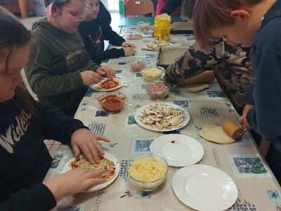 Wychowankowie z PWD z Lasek formują i dodają składniki na pizzę.