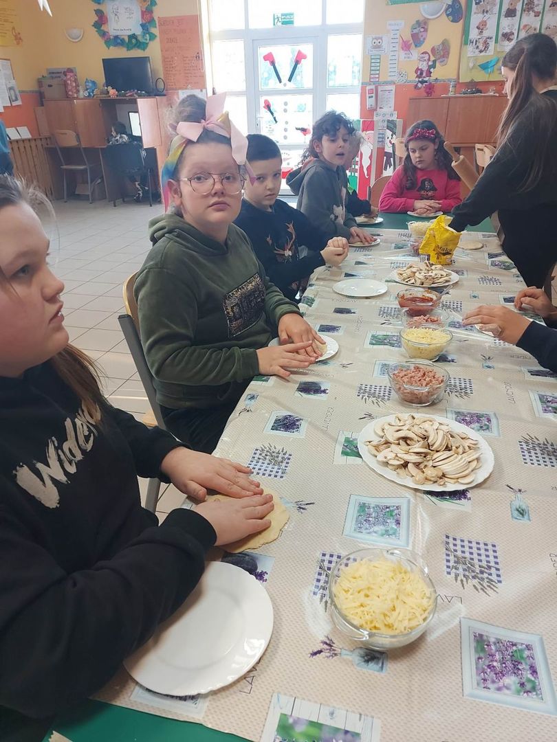 Wychowankowie z PWD z Lasek formują i dodają składniki na pizzę.
