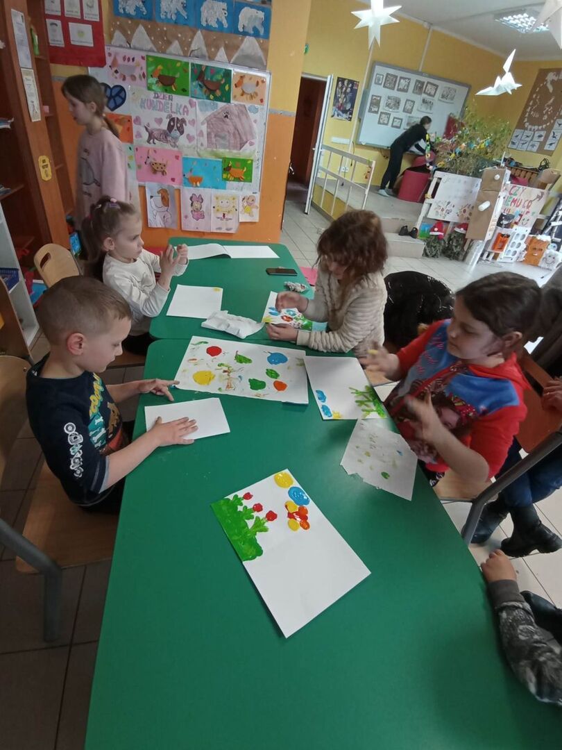 Dzieci z PWD z Lasek malują wiosenne obrazy paluszkami i farbami.