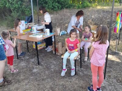 Kobieta zaplata dziewczynce warkoczyk. Dzieci czekające w kolejce.